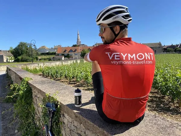 A cyclist wearing a Veymont Travel jersey, sitting facing the Meursault vineyards in Burgundy
